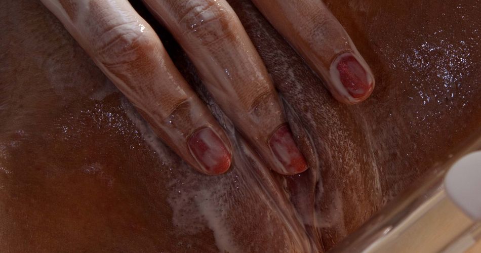 Close up image of Nikki playing with her genitals covered in lotion.